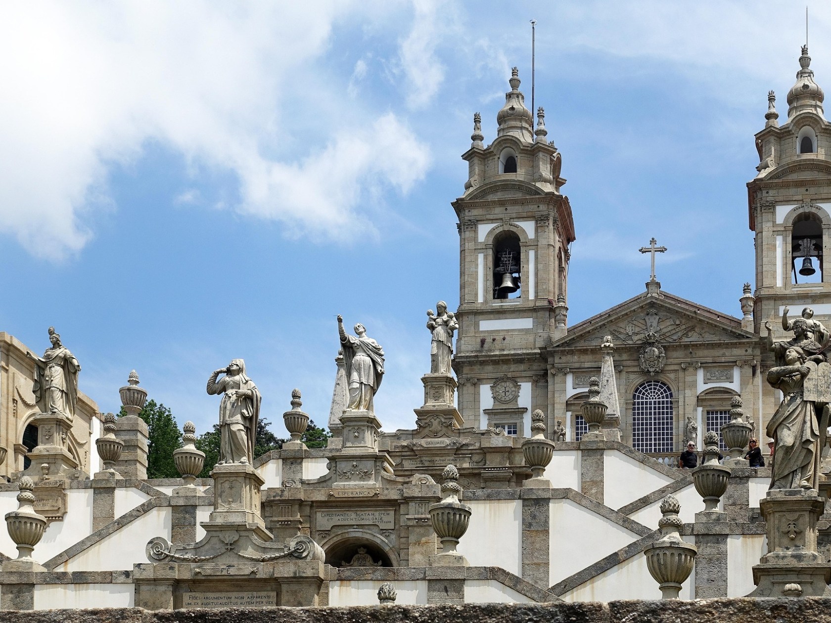 Baroque church facade with stone statues and ornate details under a blue sky.