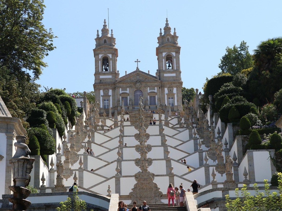 Ornate staircase leading to a church with two bell towers, surrounded by greenery.