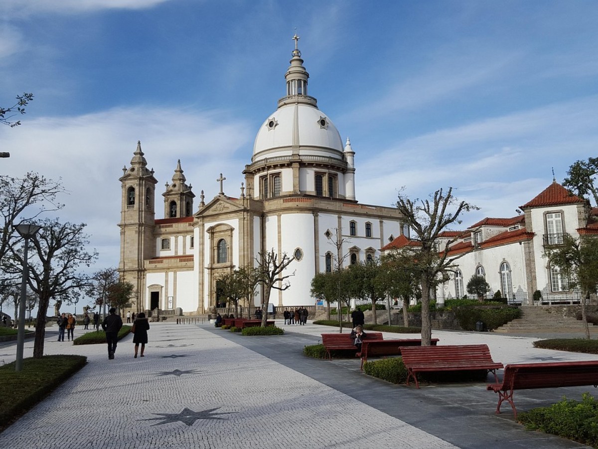 People walking near a large white domed church with a stone facade and trees around.