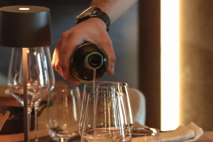 Person pouring wine at a dinner table with food and glasses.