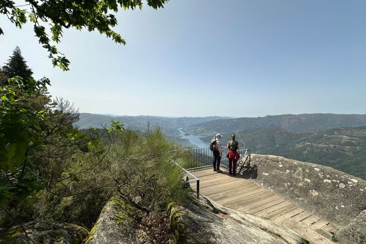 Three people on a wooden viewing platform overlooking a vast, hilly landscape and river.