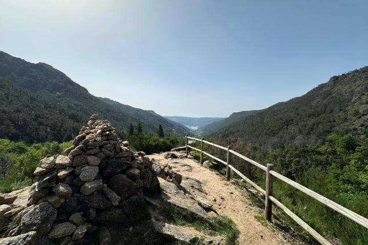 Scenic view of a mountain valley with a stone cairn and wooden fence.
