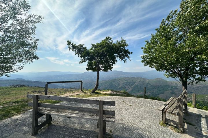 Mountain viewpoint with benches, trees, and a scenic valley view.