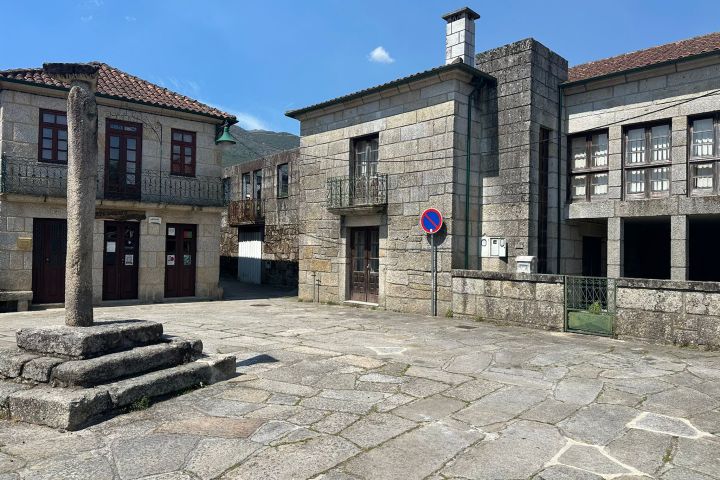 Stone buildings around a cobblestone square with a stone pillar and a no parking sign.