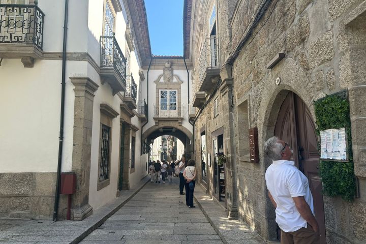 Narrow stone street with archway, people walking, historic buildings.