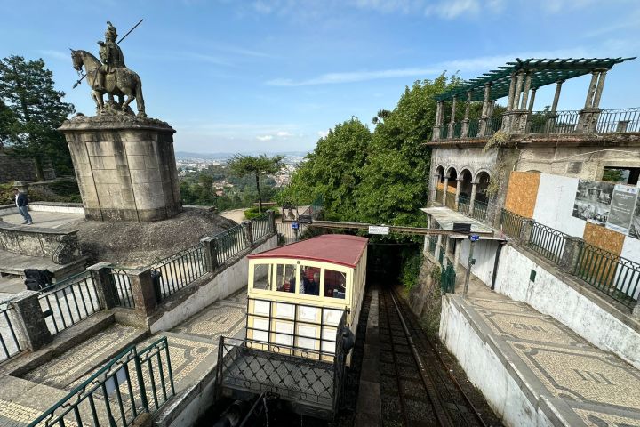 Funicular station with statue, stone path, rail tracks, and trees.