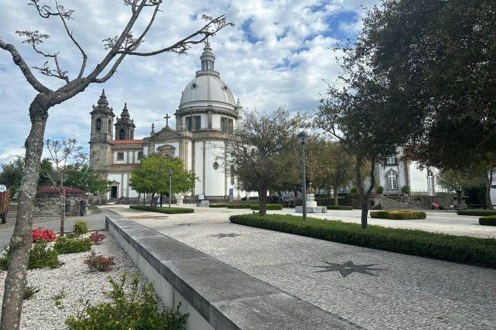 Historic church with dome, trees, and paved courtyard under cloudy sky.