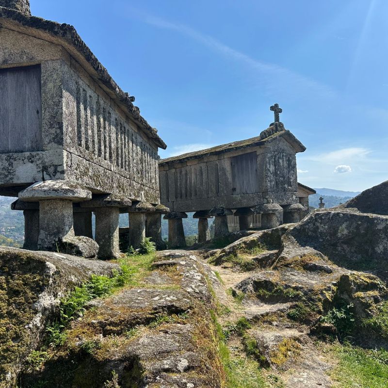 Stone granaries on stilts with a cross on a sunny day.