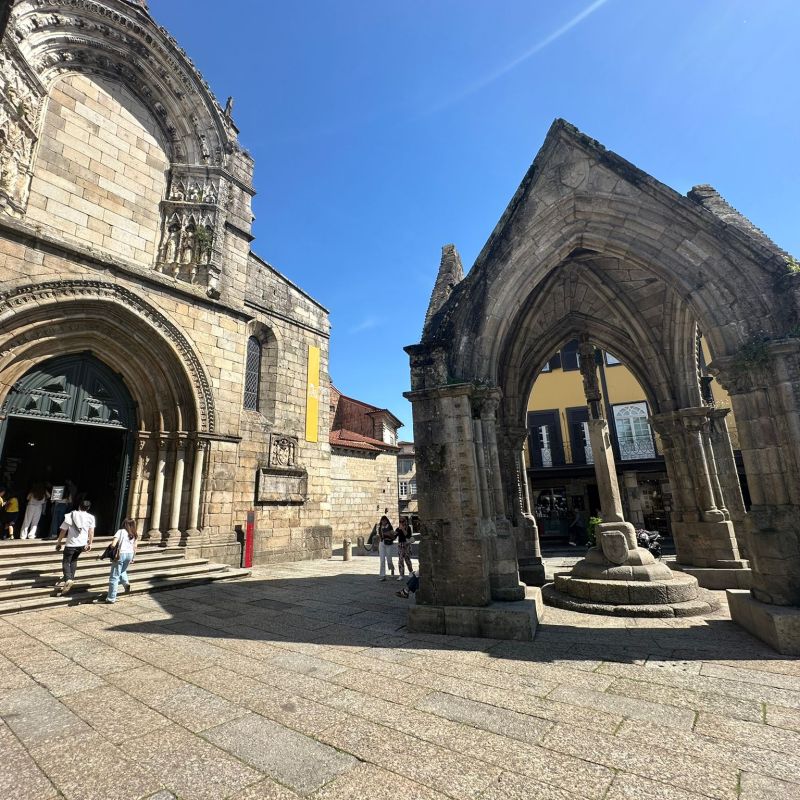 Historic stone church and arch in sunny courtyard with people.
