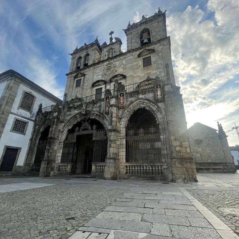Historic stone cathedral with twin towers and arches against a cloudy sky.