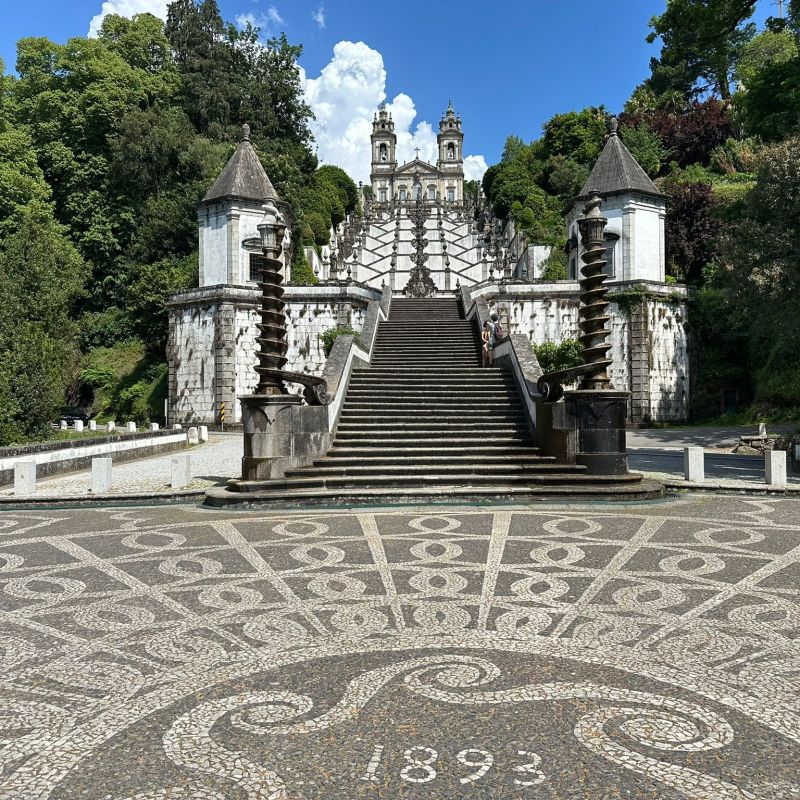 Intricate stone staircase with ornate design, tall columns, and lush greenery in the background.