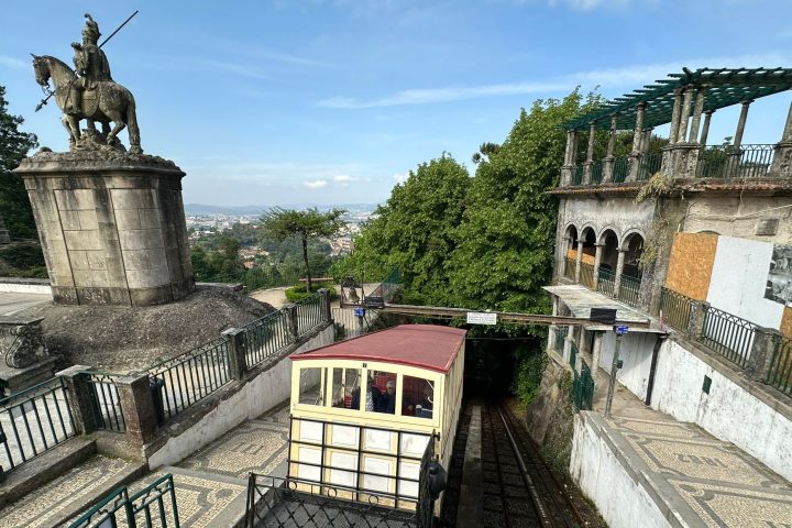 Funicular near a statue of a rider on horseback and trees on a clear day.